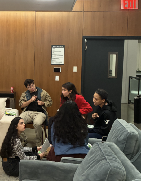 A group of five people engaged in conversation in a cozy indoor setting.
